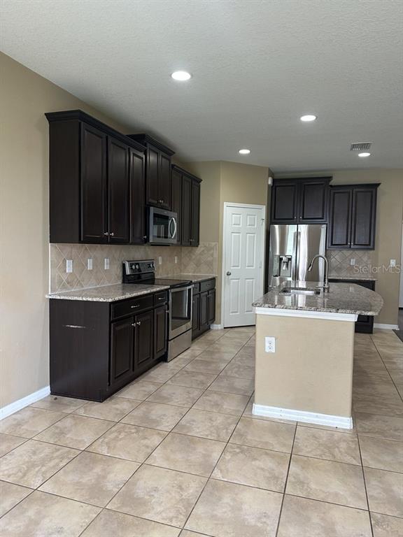 A kitchen features dark wood cabinets, granite countertops, stainless steel appliances, and tile flooring — 3034 WINGLEWOOD CIRCLE, LUTZ, FL