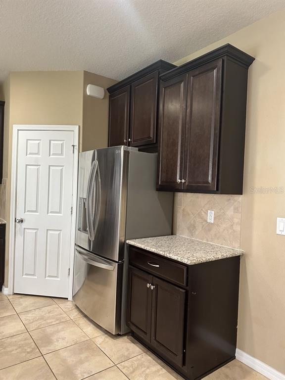 A kitchen area features dark wood cabinets, a stainless steel refrigerator, and granite countertops — 3034 WINGLEWOOD CIRCLE, LUTZ, FL