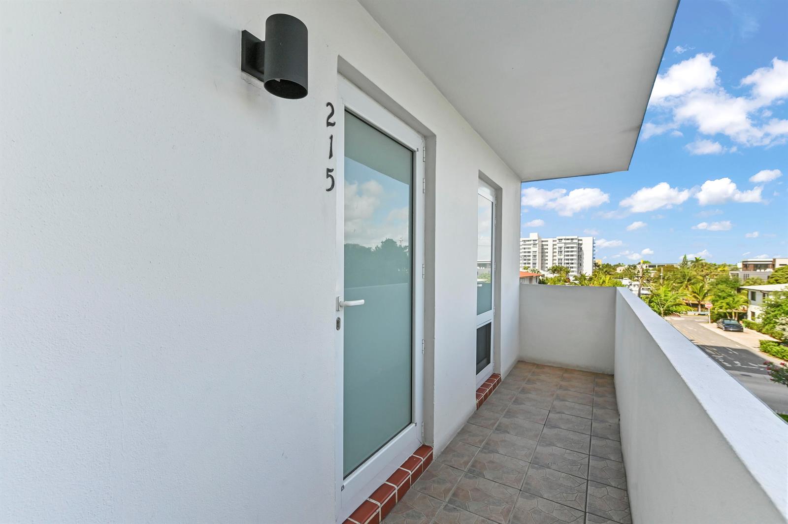 A white exterior balcony features a tiled floor, a glass door numbered 215, and lighting — 1630 N Ocean Boulevard # 215, Pompano Beach FL 33062, POMPANO BEACH, FL