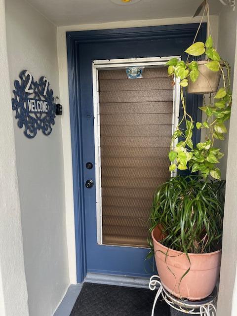 A blue front door with a brown shade and hanging and potted plants — 27 Capri # A, Delray Beach FL 33484, DELRAY BEACH, FL
