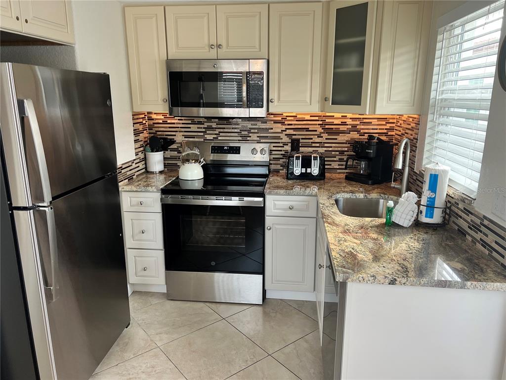 A kitchen features stainless steel appliances, cream cabinets, granite countertops, and a tiled backsplash — 6154 MIDNIGHT PASS ROAD UNIT B07, SARASOTA, FL