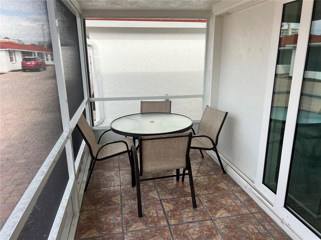 A screened-in patio features a round glass table with four chairs on tiled flooring — 6154 MIDNIGHT PASS ROAD UNIT B07, SARASOTA, FL