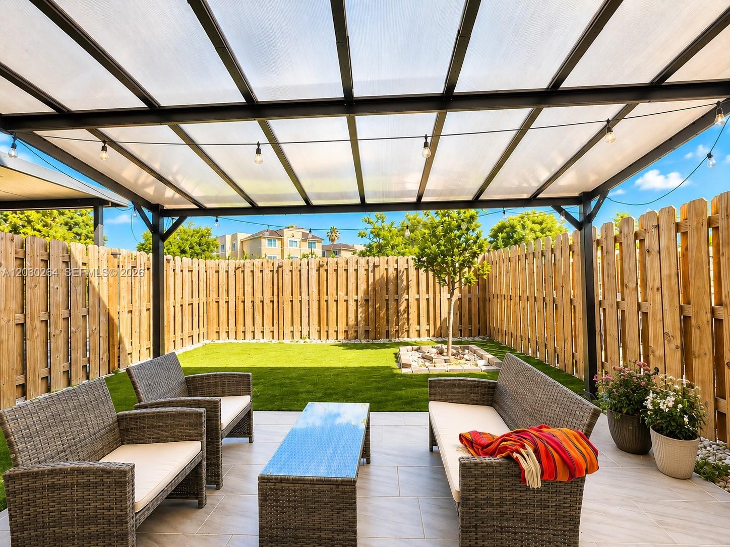A covered patio features wicker furniture on tiled flooring overlooking a fenced-in grassy yard — 12159 NW 23rd Ct # 12159, Miami FL 33167, MIAMI, FL