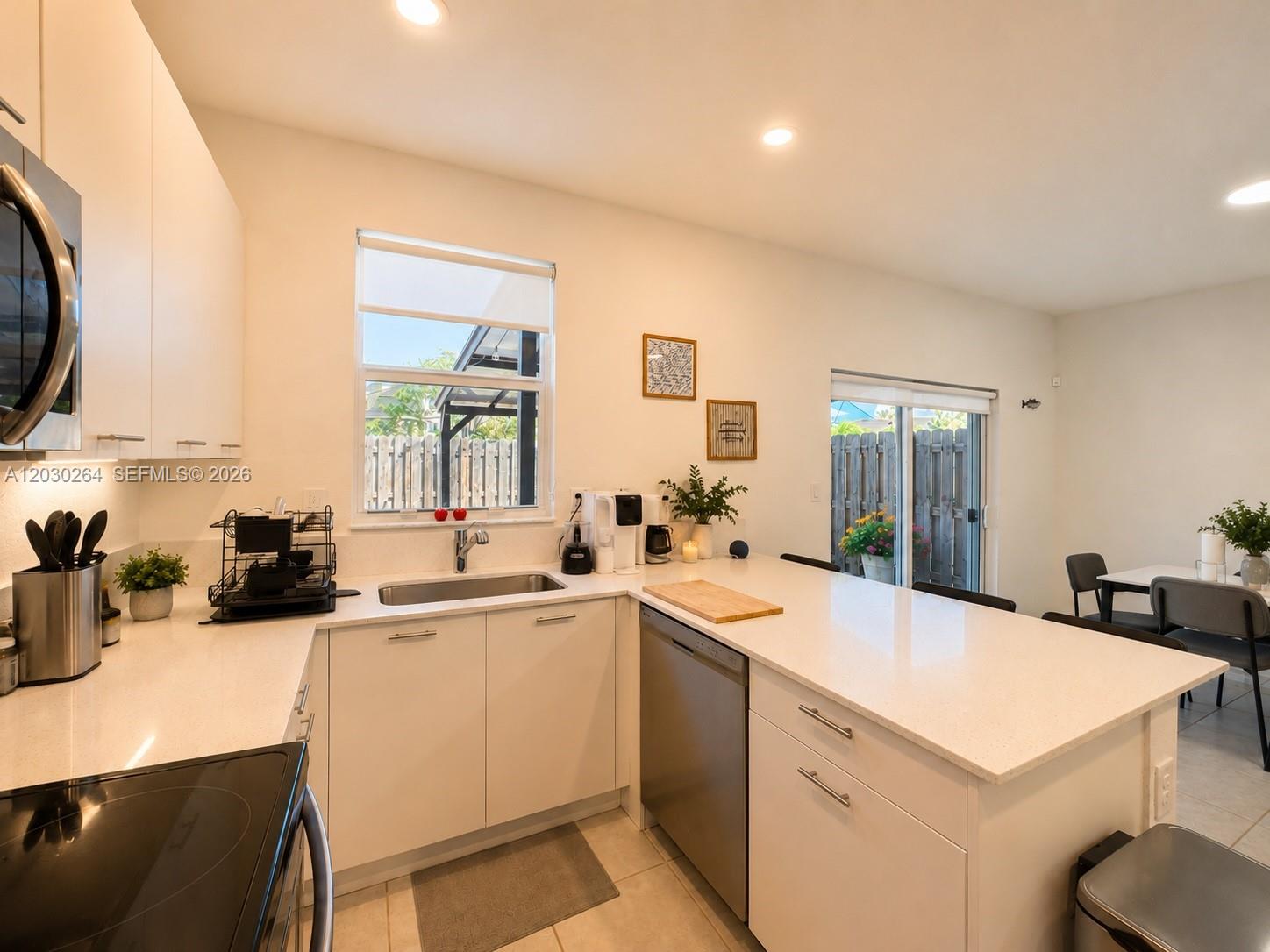 A modern kitchen features white cabinets, quartz countertops, stainless steel appliances, and a sliding glass door — 12159 NW 23rd Ct # 12159, Miami FL 33167, MIAMI, FL