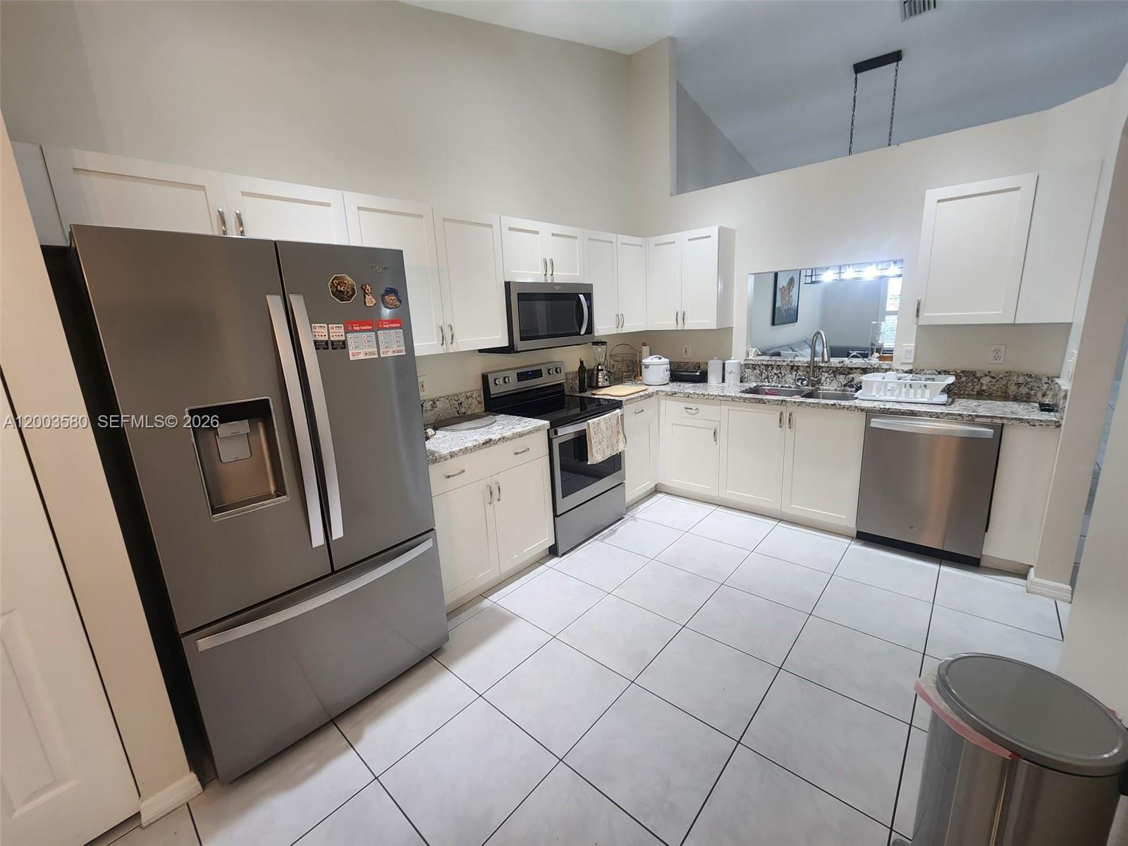 A kitchen features white cabinets, granite countertops, stainless steel appliances, and light-colored tile flooring — 6053 Heliconia Rd, Delray Beach FL 33484, DELRAY BEACH, FL