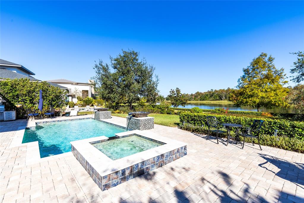 A backyard features a swimming pool, a raised spa, and a patio overlooking a lake — 14153 CORRIGAN AVENUE, ORLANDO, FL