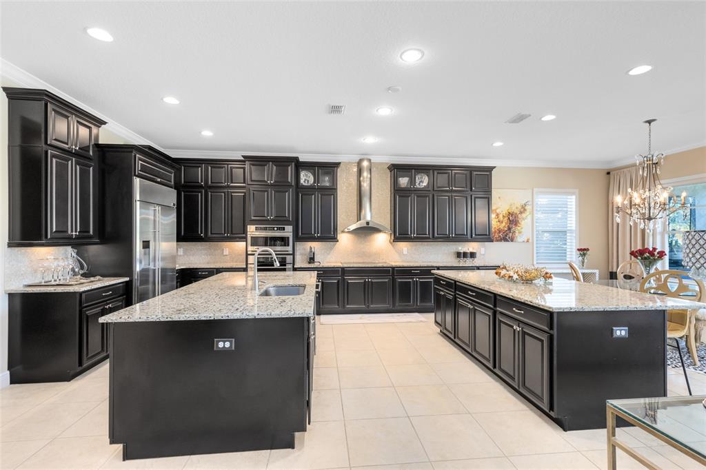 A spacious kitchen features dark cabinetry, granite countertops, two large islands, and stainless steel appliances — 14153 CORRIGAN AVENUE, ORLANDO, FL
