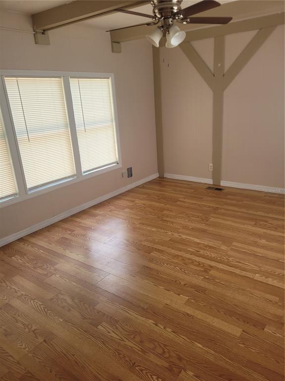 An empty room features wood-look flooring, a ceiling fan, and decorative wall beams — 13164 SE 102ND TERRACE, OCKLAWAHA, FL