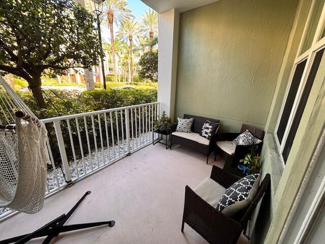 A covered balcony features a hanging chair, wicker patio furniture, and a view of palm trees — 804 E Windward Way # 103, Lantana FL 33462, LANTANA, FL
