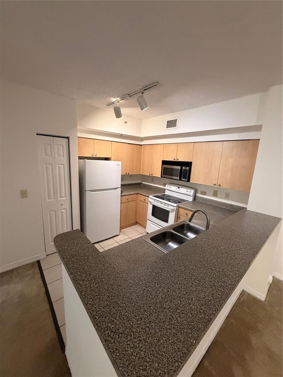 A kitchen features light wood cabinets, white appliances, and a dark speckled countertop peninsula — 2351 W Preserve Way # 104, Miramar FL 33025, MIRAMAR, FL