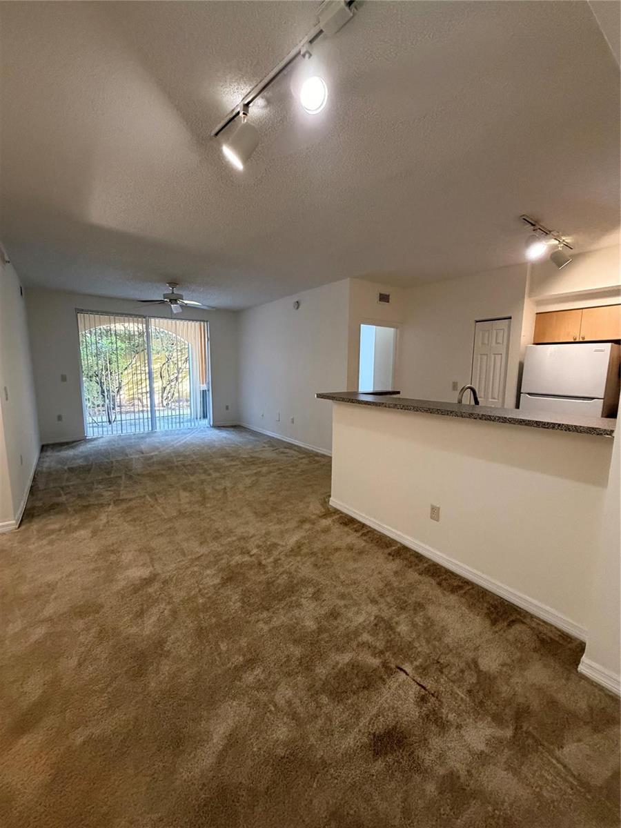 An open-concept living area with beige carpet, a breakfast bar, and a sliding glass door — 2351 W Preserve Way # 104, Miramar FL 33025, MIRAMAR, FL
