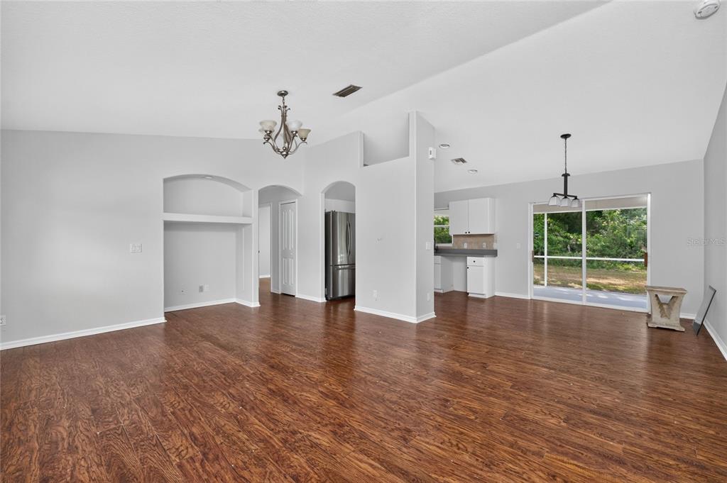 An open-concept living and dining area features dark wood flooring, white walls, and vaulted ceilings — 4436 MAURBACH TERRACE, NORTH PORT, FL