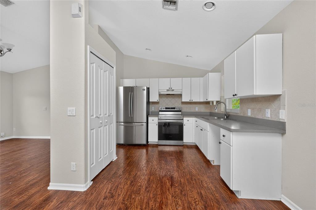 A kitchen with white cabinets, stainless steel appliances, gray countertops, and dark wood flooring — 4436 MAURBACH TERRACE, NORTH PORT, FL
