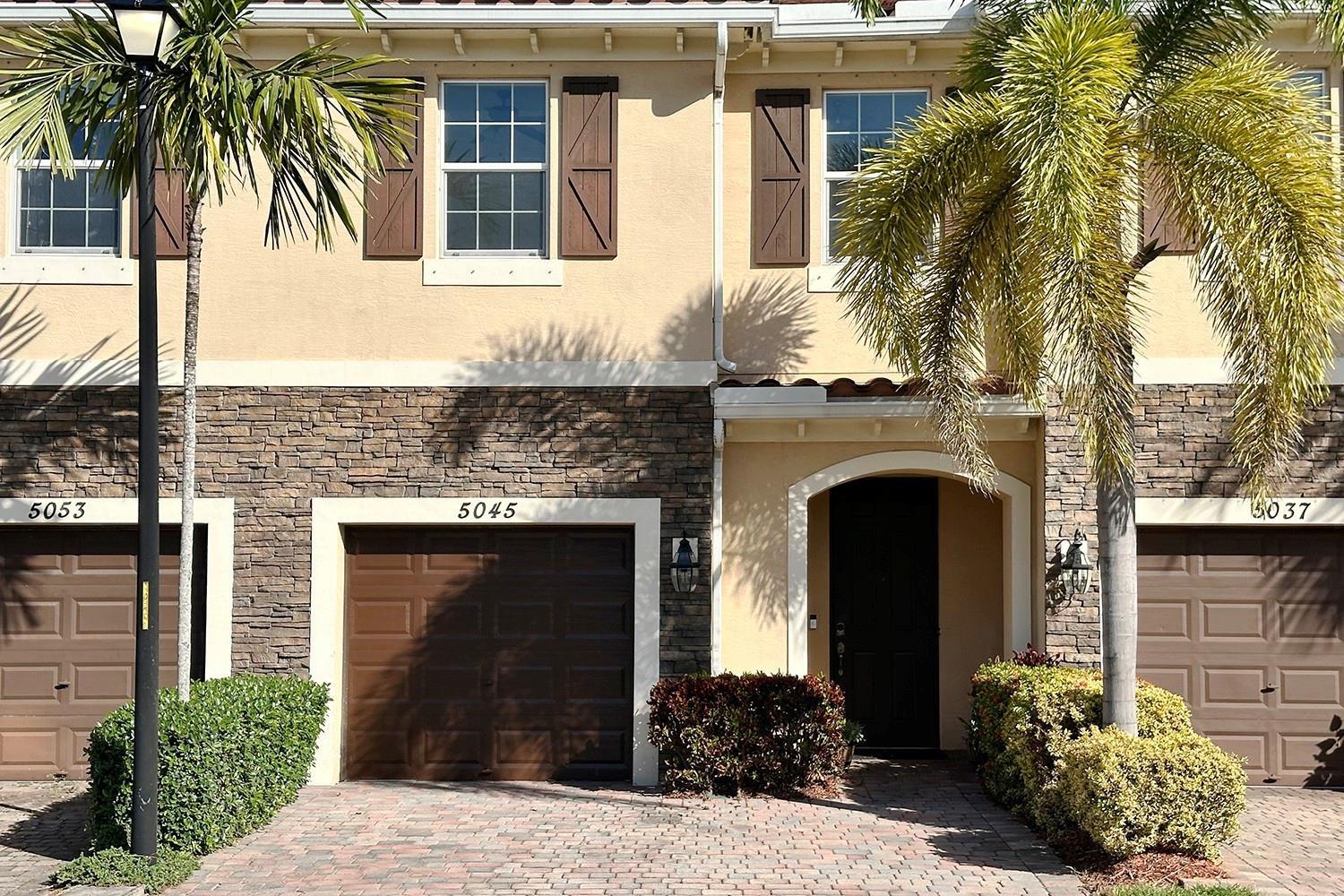 A two-story townhouse exterior features a stone facade, brown garage doors, and palm trees — 5045 Ellery Terrace, West Palm Beach FL 33417, WEST PALM BEACH, FL