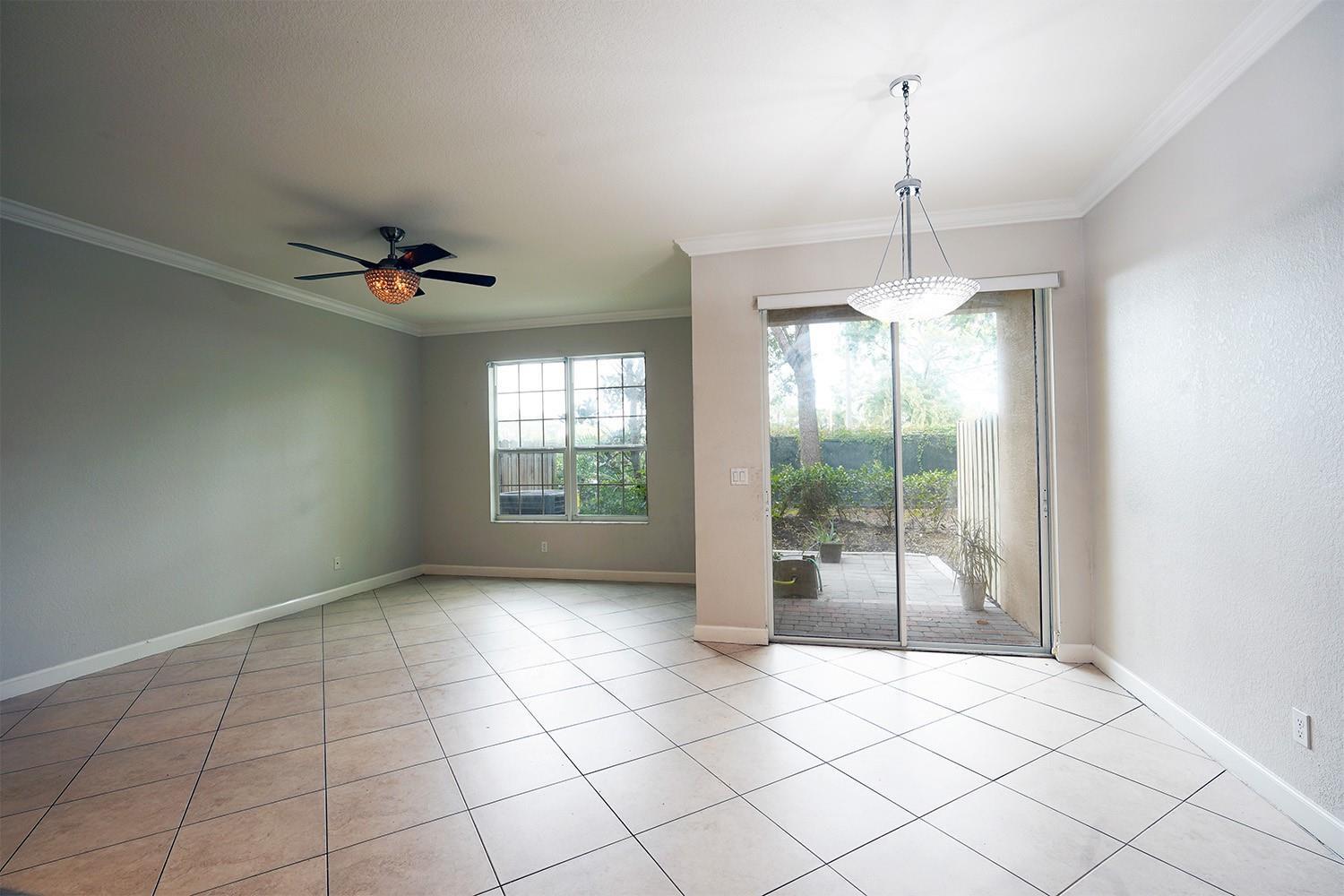 An empty room with tile flooring, a ceiling fan, a chandelier, and sliding glass doors — 5045 Ellery Terrace, West Palm Beach FL 33417, WEST PALM BEACH, FL