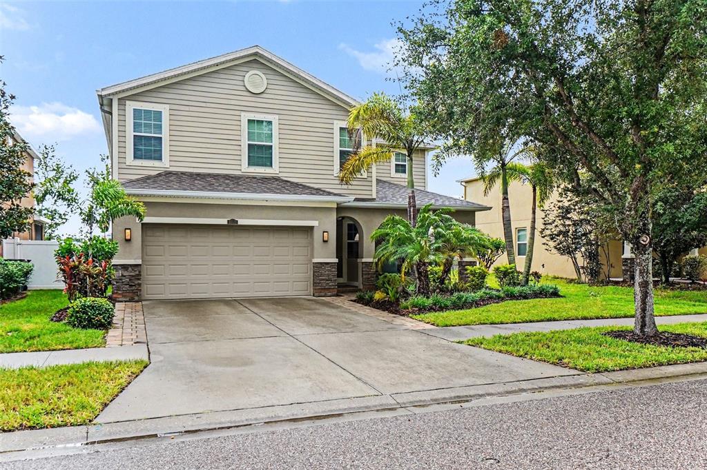 A two-story suburban house with beige siding, a two-car garage, and a landscaped front yard — 10511 AVIAN FORREST DR, RIVERVIEW, FL