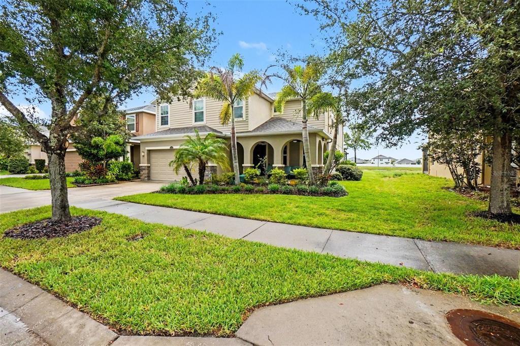 A two-story suburban house with a tan exterior, arched entryway, and palm trees in front — 10511 AVIAN FORREST DR, RIVERVIEW, FL