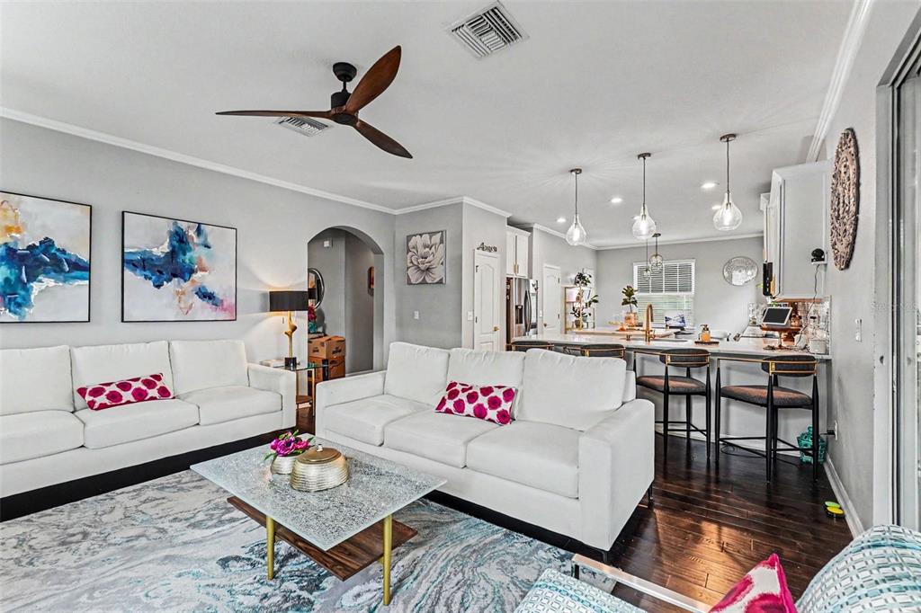 A living room with white sofas and a kitchen with bar seating on dark floors — 10511 AVIAN FORREST DR, RIVERVIEW, FL