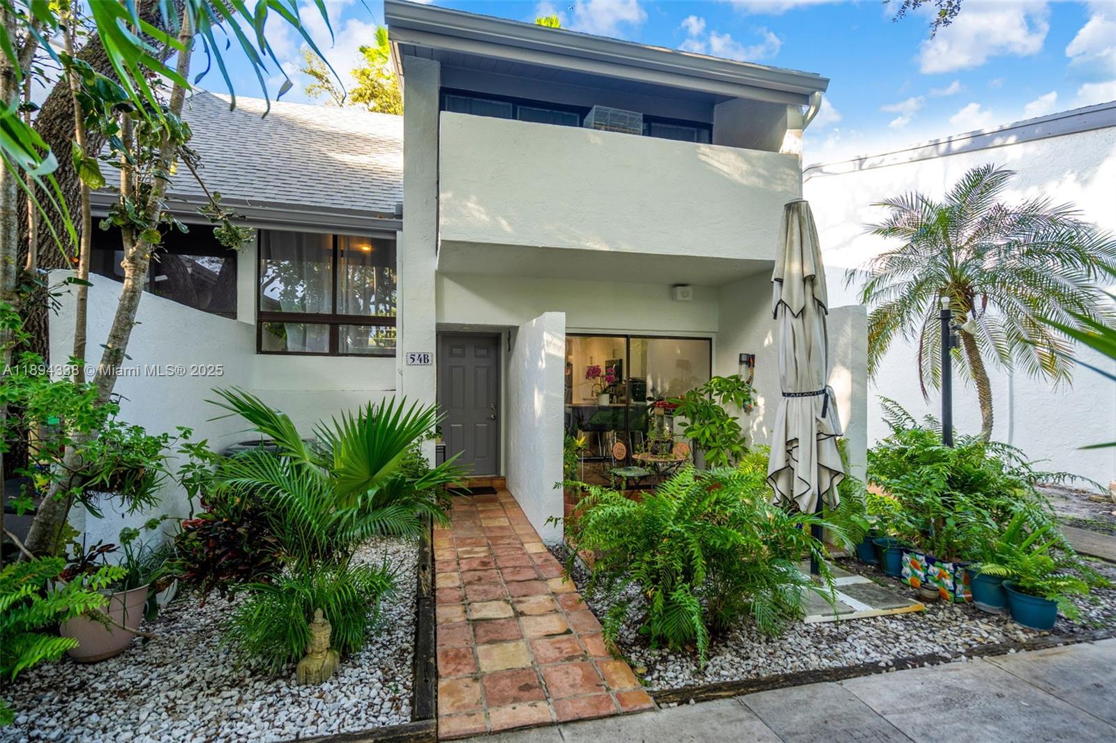 A two-story townhouse exterior features a tiled walkway, a front door, and lush landscaping — 19440 NE 26th Ave # 54B, Miami FL 33180, MIAMI, FL