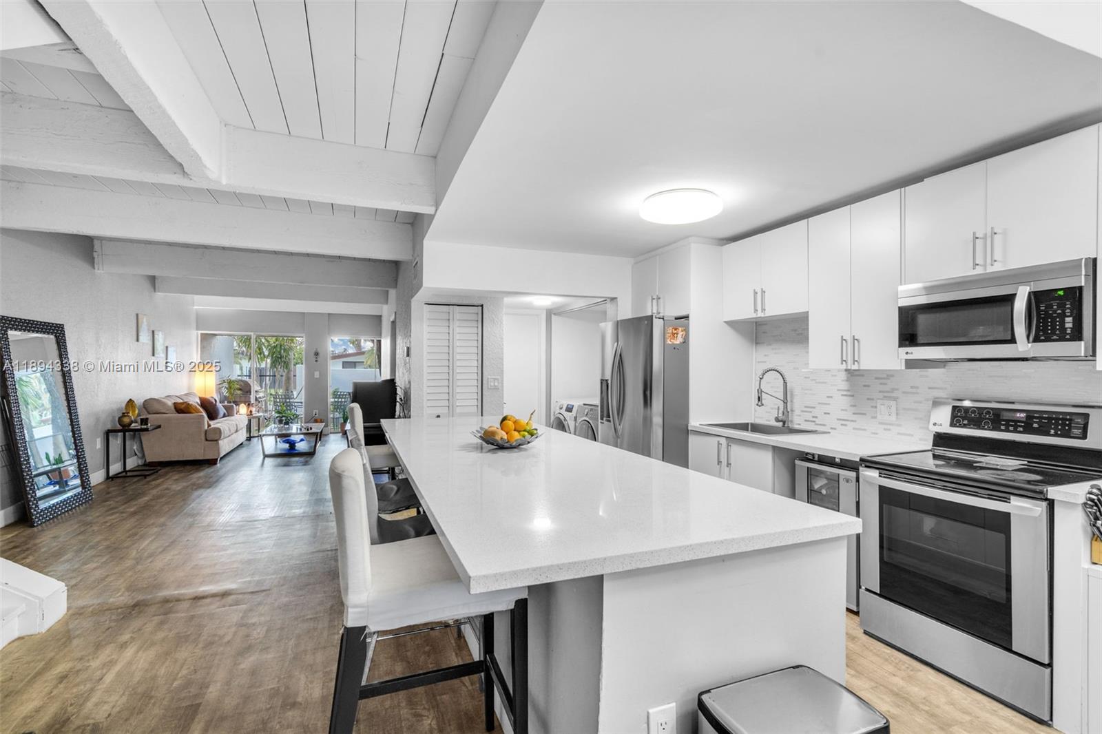 A modern kitchen with white cabinets and a long island overlooks an open living area — 19440 NE 26th Ave # 54B, Miami FL 33180, MIAMI, FL