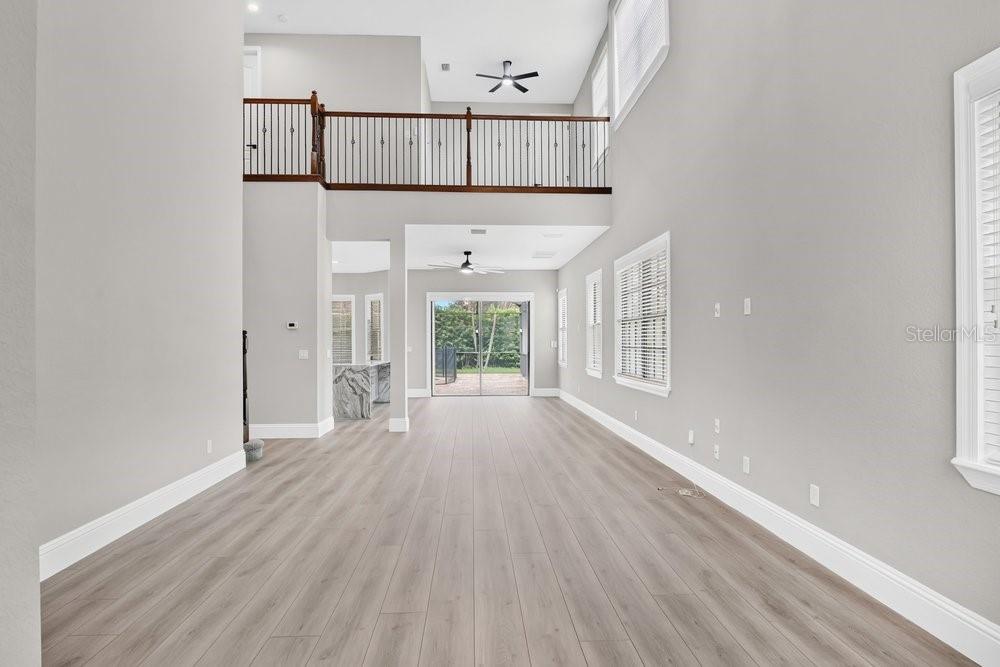 A spacious living area with high ceilings, light wood-look flooring, and a second-story balcony railing — 10459 STAPELEY DRIVE, ORLANDO, FL