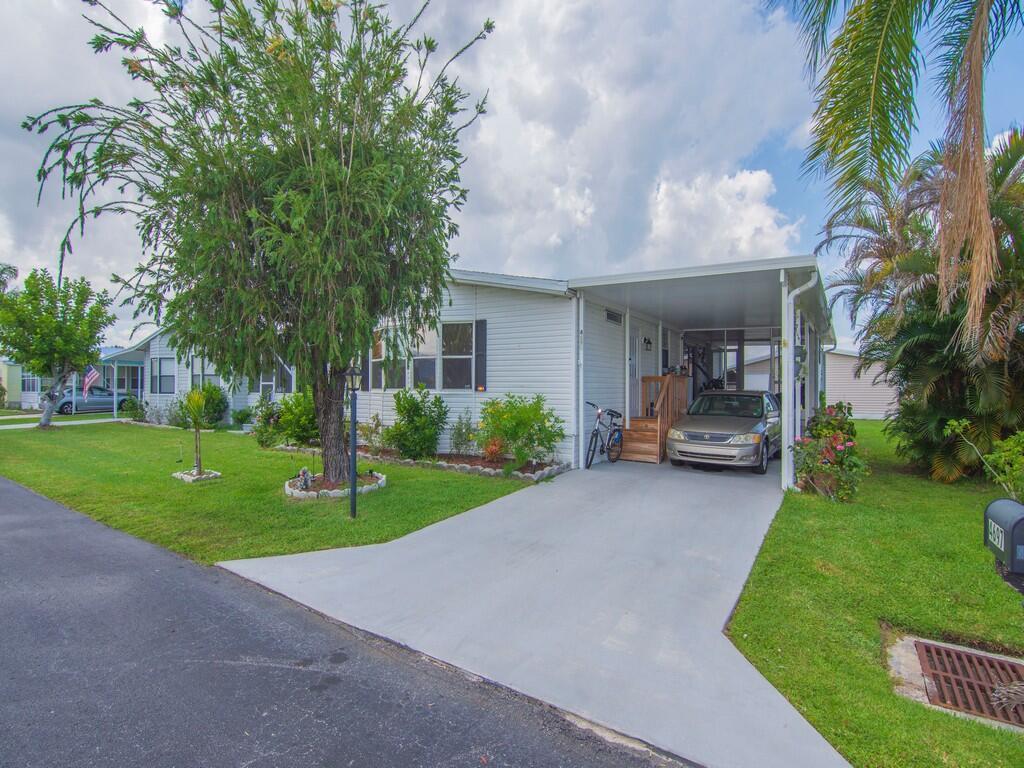 A single-story mobile home with a carport, driveway, and a large tree in the front yard — 4697 SE Copperwood Terrace, Stuart FL 34997, STUART, FL