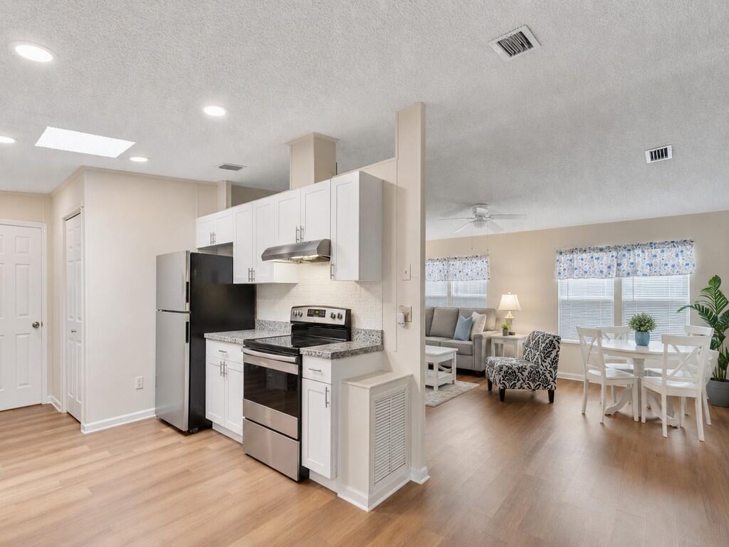 A kitchen with white cabinets and stainless steel appliances opens into a living and dining area — 4697 SE Copperwood Terrace, Stuart FL 34997, STUART, FL