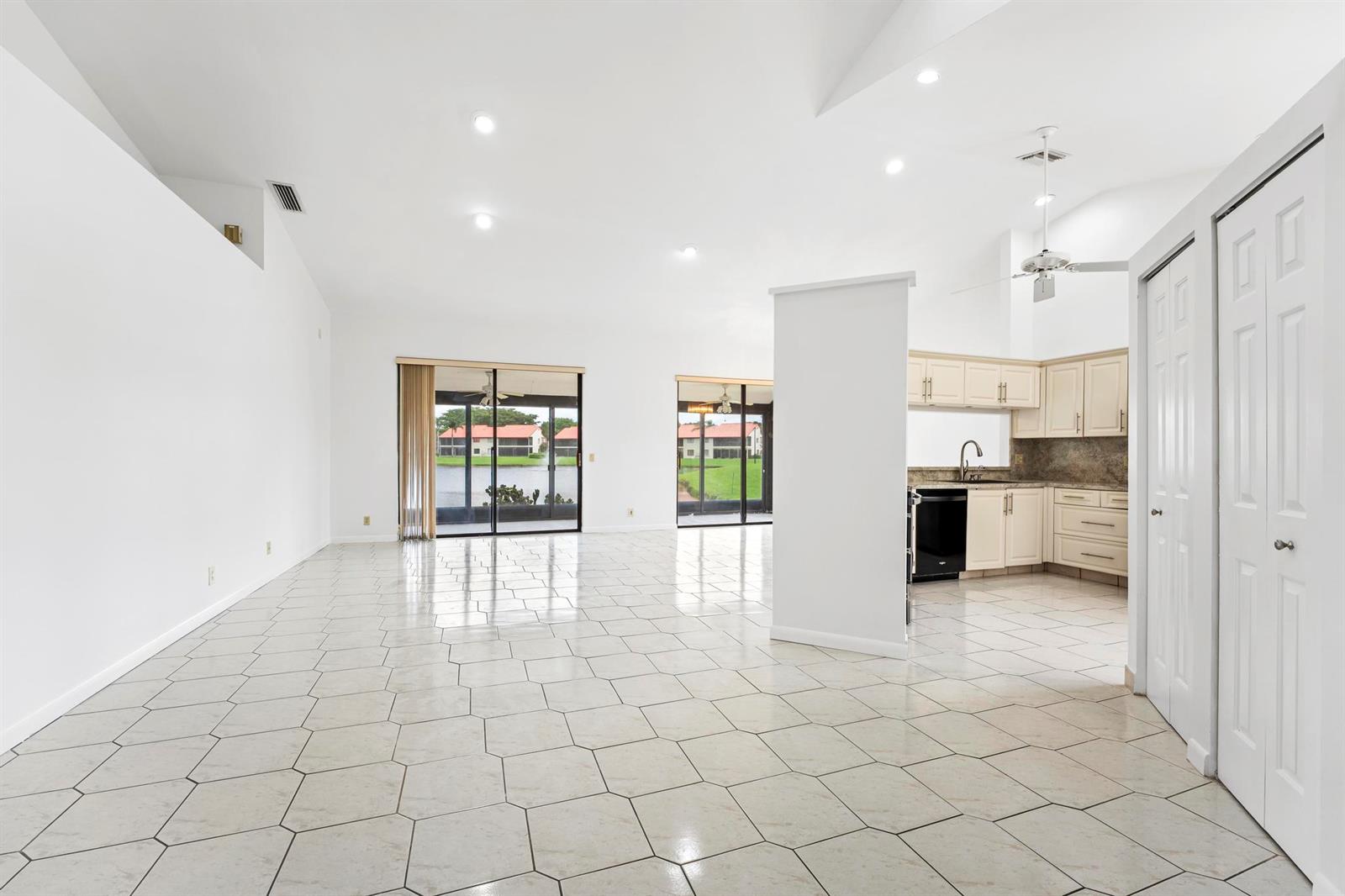 An open-concept living area with white tile floors, vaulted ceilings, and a kitchen with cabinets — 7792 Lexington Club Boulevard # B, Delray Beach FL 33446, DELRAY BEACH, FL