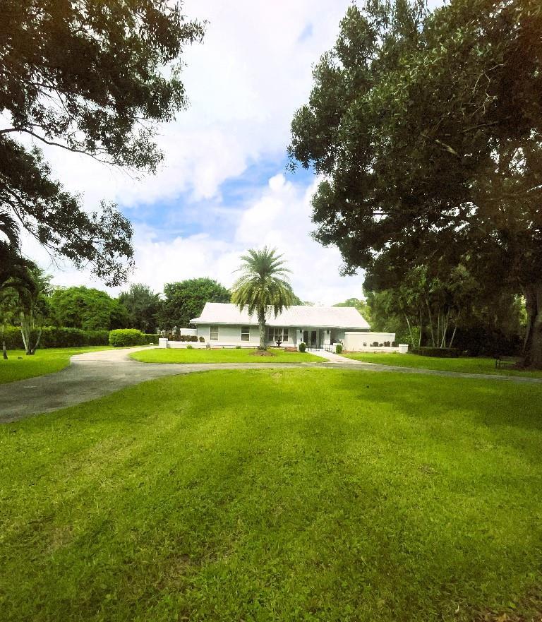 A single-story house with a white exterior sits behind a large lawn and palm tree — 14183 Greentree Trail, Wellington FL 33414, WELLINGTON, FL