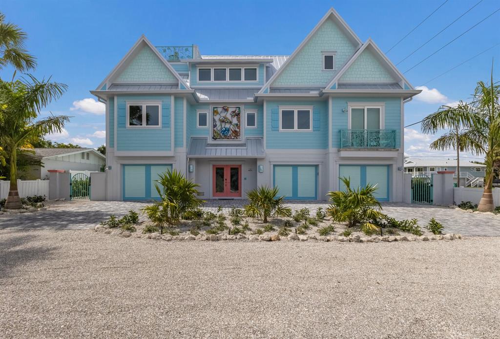 A three-story light blue house with a coral front door and three garage bays — 118 MANGROVE AVENUE, ANNA MARIA, FL