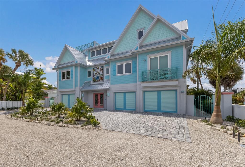 A light blue, three-story coastal house with a paved driveway and a pink front door — 118 MANGROVE AVENUE, ANNA MARIA, FL