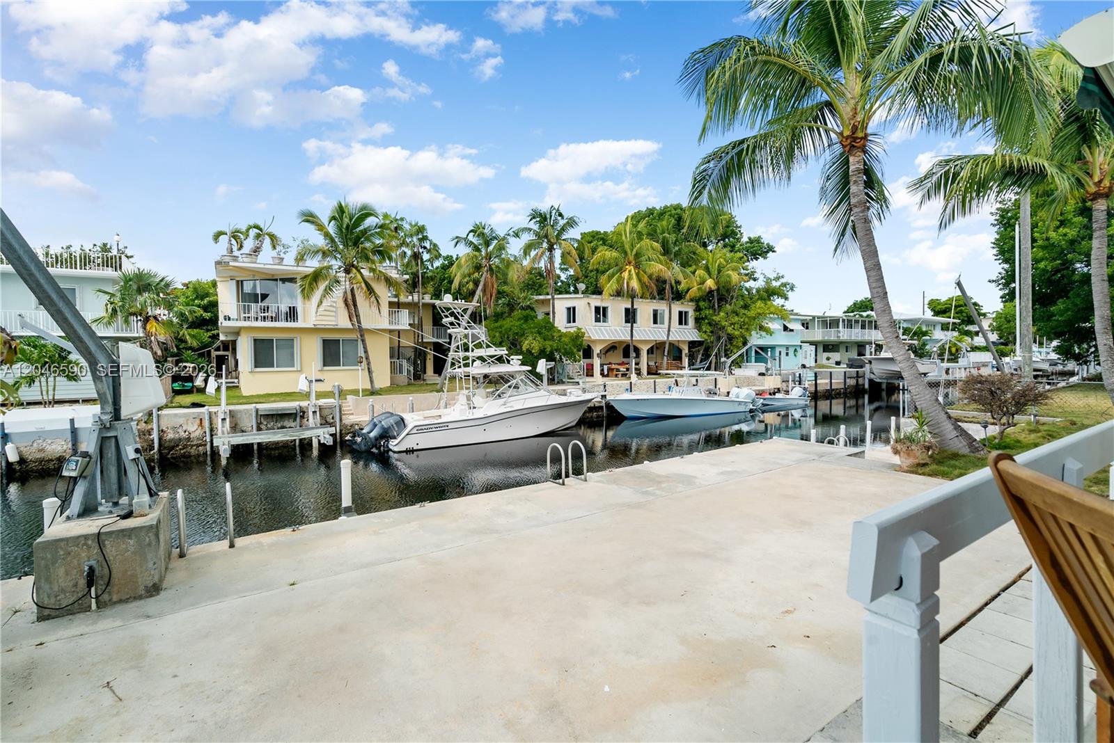 A concrete dock overlooks a canal with two boats moored in front of yellow houses — 1210 Cactus St, Key Largo FL 33037, KEY LARGO, FL