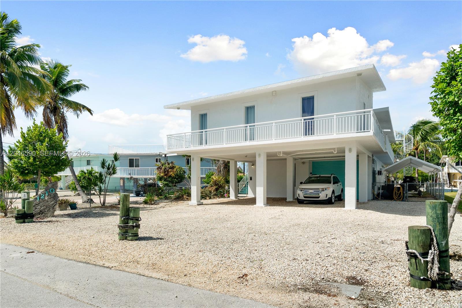 A white two-story stilt house features a gravel driveway and a covered parking area — 1210 Cactus St, Key Largo FL 33037, KEY LARGO, FL