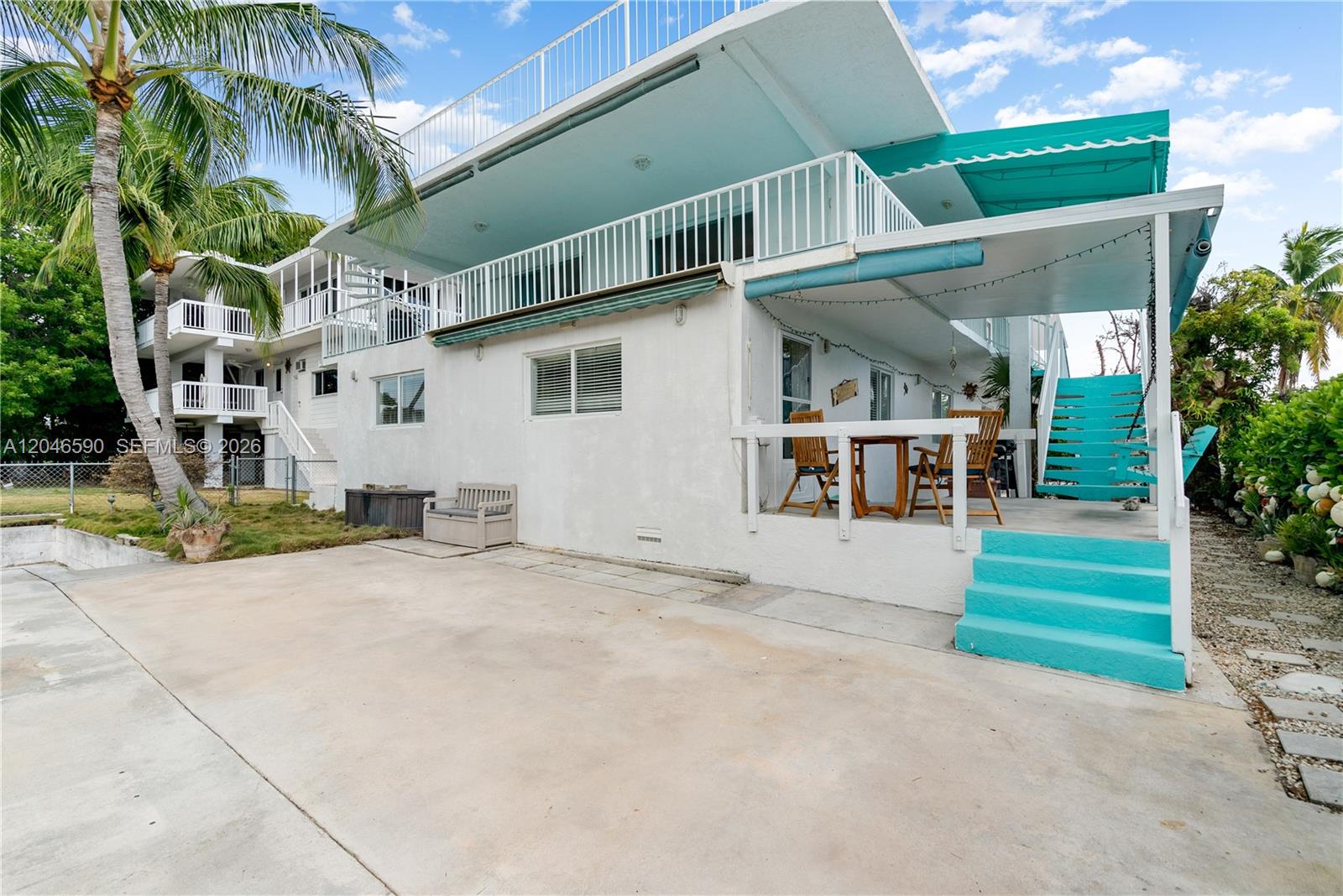 A white two-story house features a turquoise staircase, a covered patio, and a balcony — 1210 Cactus St, Key Largo FL 33037, KEY LARGO, FL