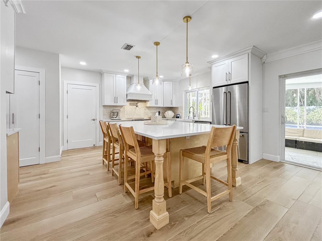 A bright kitchen features white cabinetry, a large central island with wooden stools, and light-toned flooring — 5853 LEELAND STREET S, ST PETERSBURG, FL