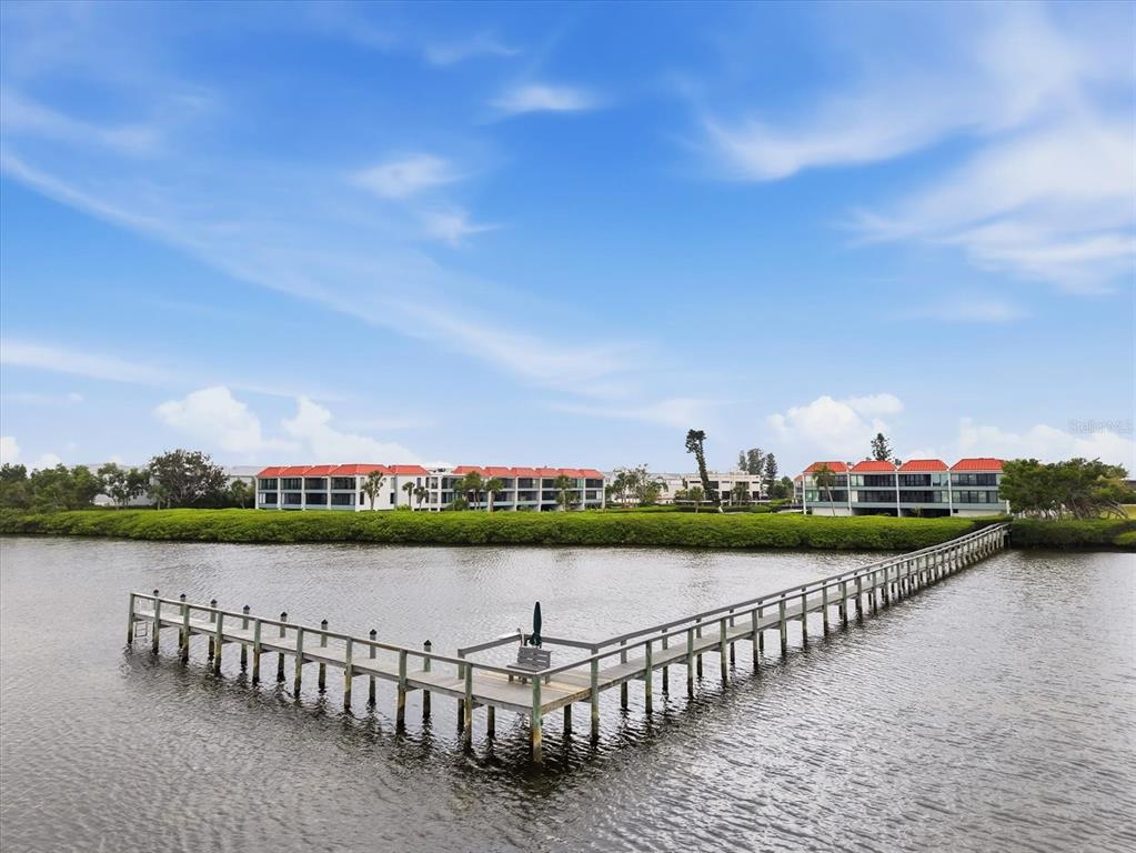 A long wooden pier extends into a calm body of water toward waterfront apartment buildings — 3705 E BAY DRIVE UNIT 117, HOLMES BEACH, FL