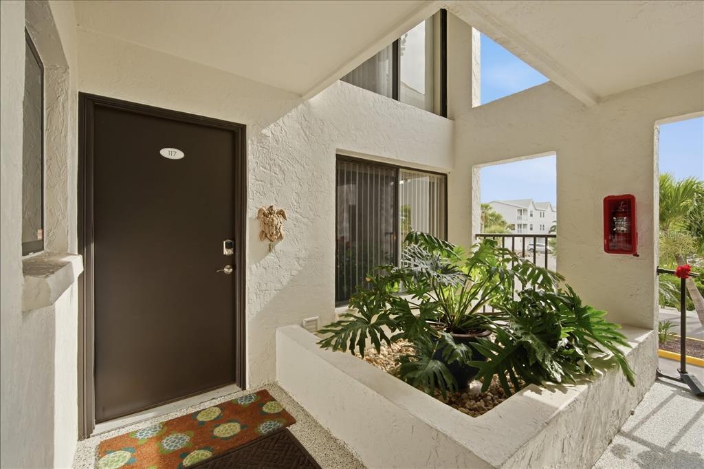 An exterior entryway features a dark brown door, a potted plant, and a fire extinguisher — 3705 E BAY DRIVE UNIT 117, HOLMES BEACH, FL