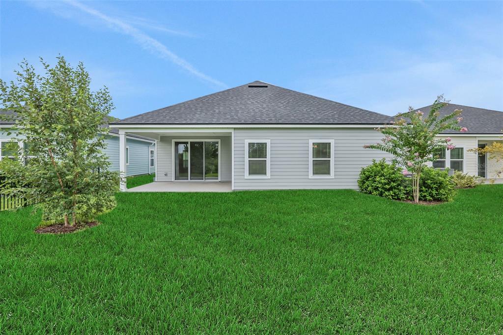 The exterior rear view of a gray house features a covered patio and green lawn — 49 WINDMILL PALM WAY, PALM COAST, FL