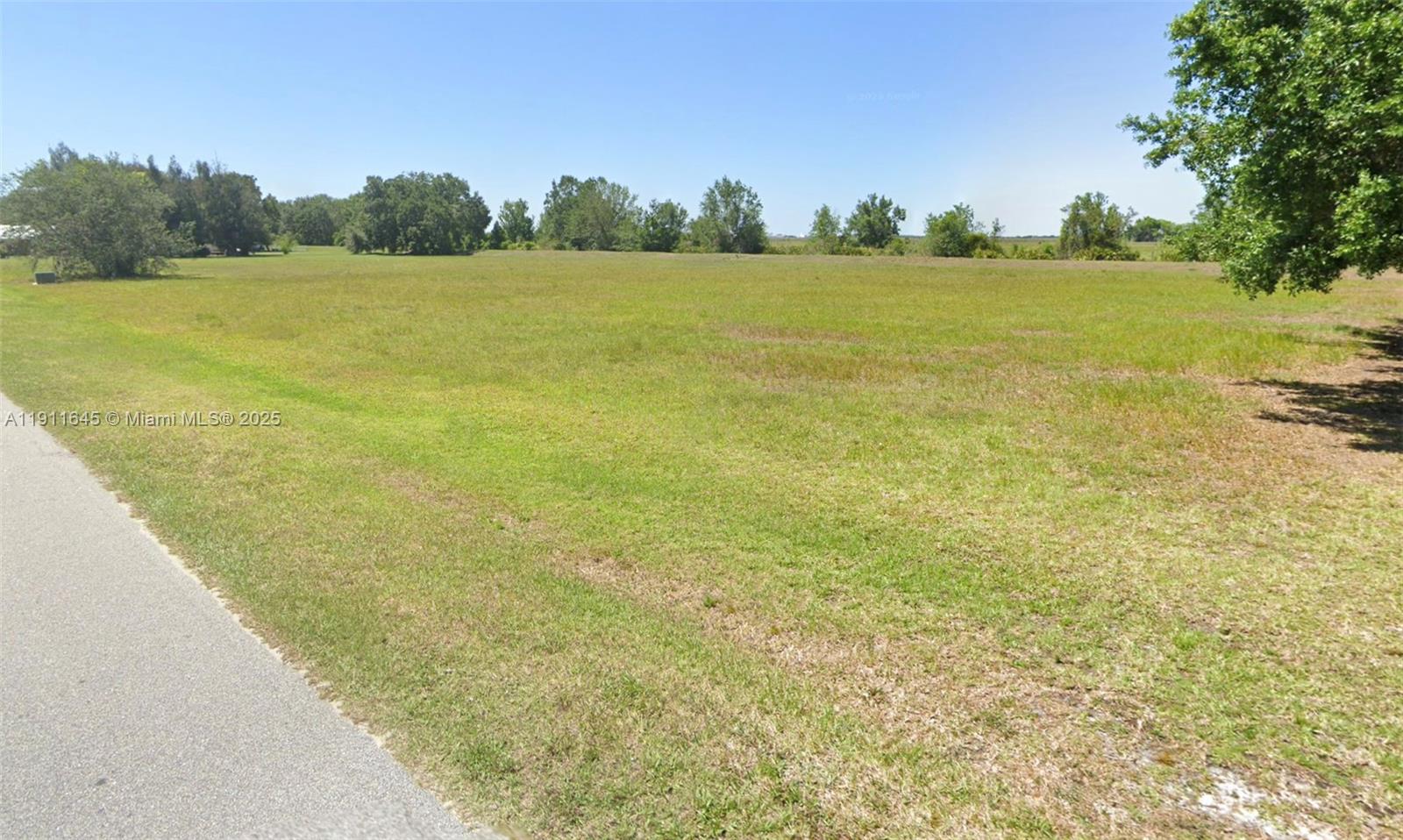 A paved road borders a large, flat, grassy vacant lot under a clear blue sky — 7109 Coral Ridge Rd, Sebring FL 33876, SEBRING, FL