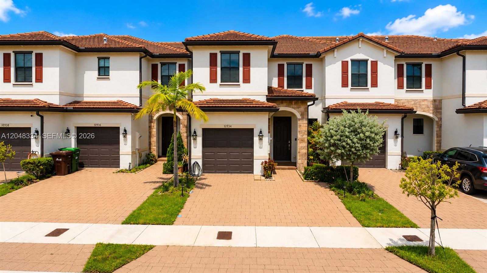 A row of three two-story townhomes features beige stucco walls, brown tile roofs, and paved driveways — 10934 W 33rd Way, Hialeah FL 33018, HIALEAH, FL