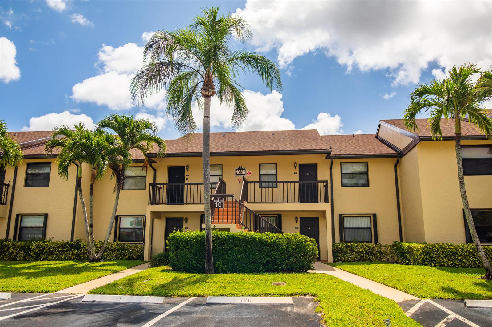 A two-story apartment building with yellow stucco walls, dark trim, and palm trees in front — 4688 Lucerne Lakes Blvd Boulevard E # 104, Lake Worth FL 33467, LAKE WORTH, FL