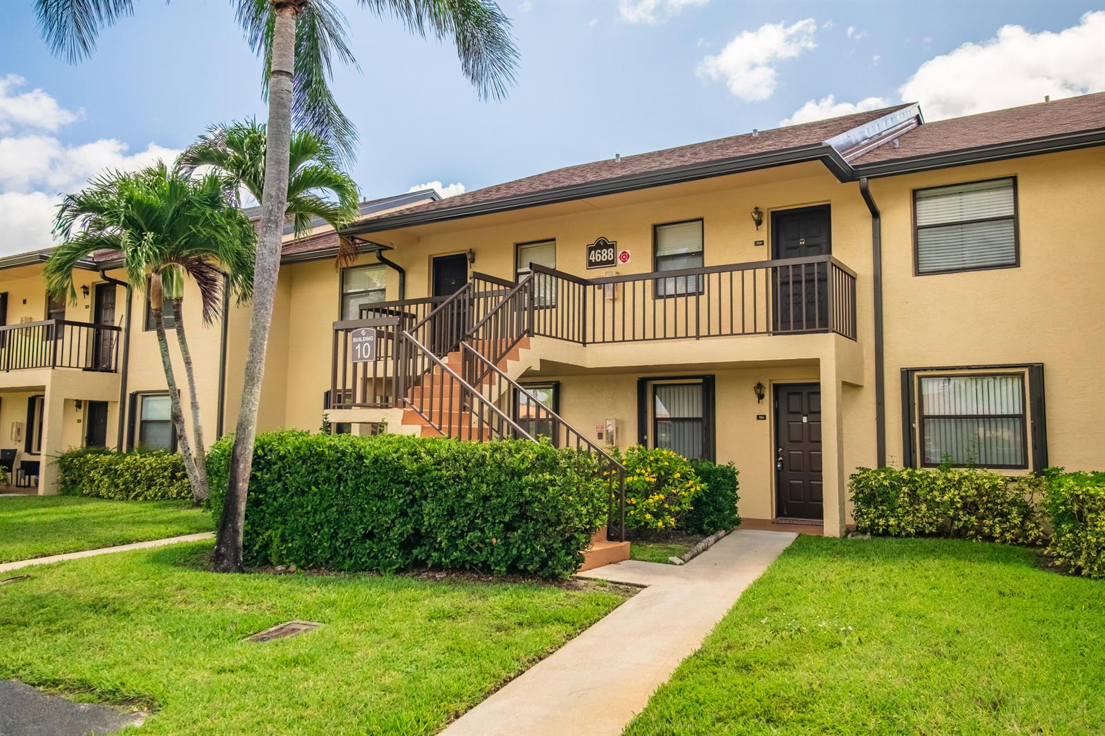 A two-story apartment building with yellow stucco walls, brown trim, and an exterior staircase — 4688 Lucerne Lakes Blvd Boulevard E # 104, Lake Worth FL 33467, LAKE WORTH, FL