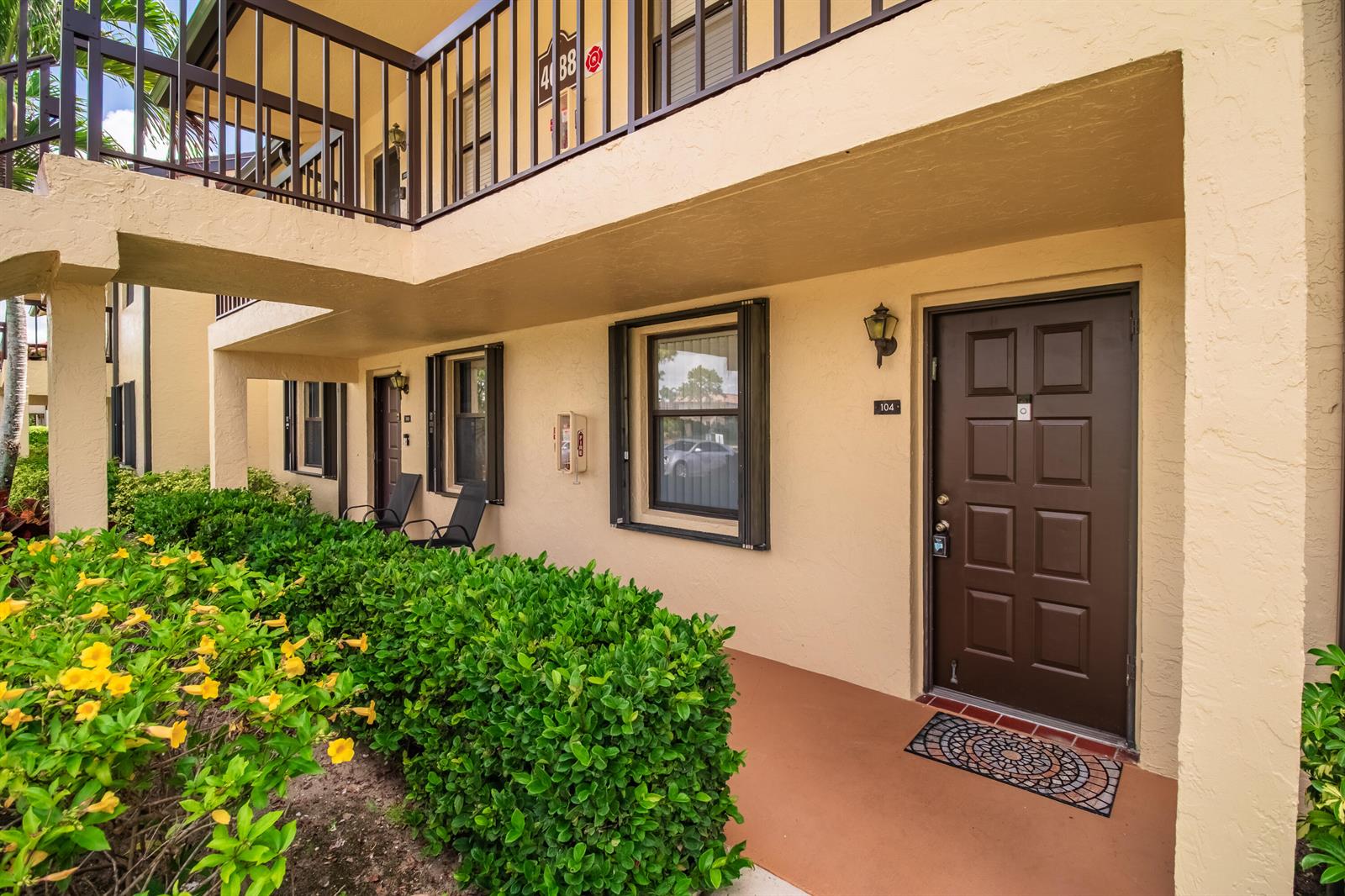 The exterior of a ground-floor apartment unit features a brown door, windows, and landscaping — 4688 Lucerne Lakes Blvd Boulevard E # 104, Lake Worth FL 33467, LAKE WORTH, FL