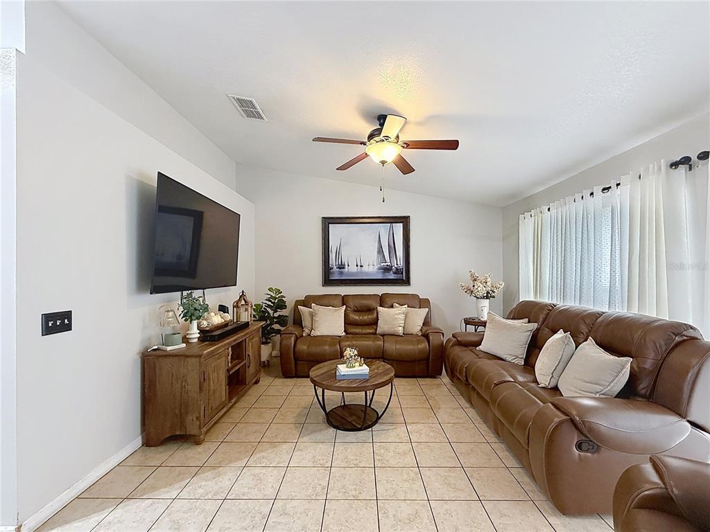 A living room features brown leather sofas, a wooden media console, and tile flooring — 522-524 IMPERIAL PLACE, KISSIMMEE, FL