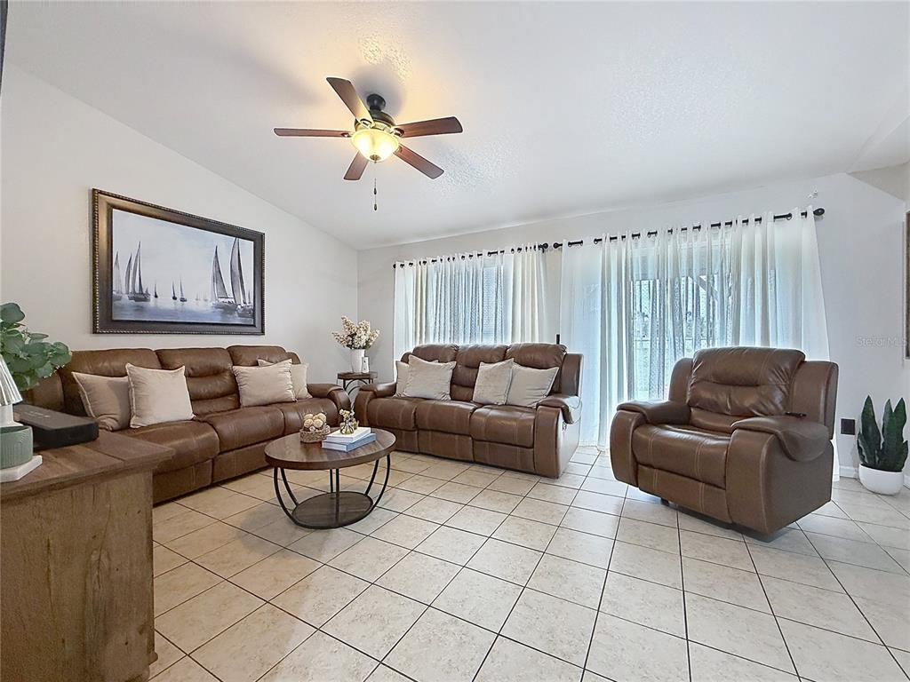 A living room features brown leather furniture, tile flooring, a ceiling fan, and large windows — 522-524 IMPERIAL PLACE, KISSIMMEE, FL