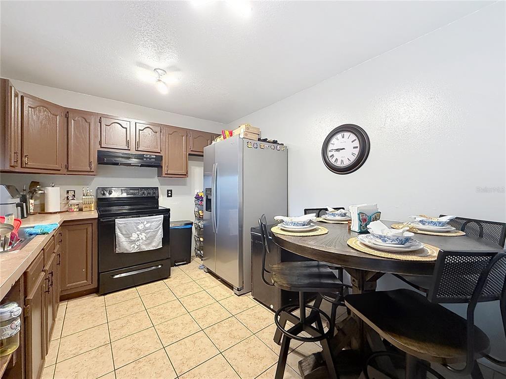 A kitchen with brown cabinets, black appliances, tile flooring, and a small dining area — 522-524 IMPERIAL PLACE, KISSIMMEE, FL