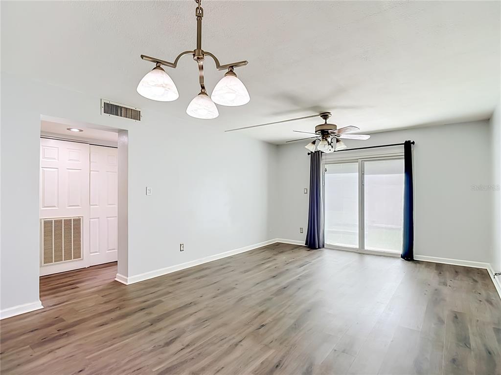 An empty room features wood-look flooring, a ceiling fan, a chandelier, and sliding glass doors — 5820 N CHURCH AVENUE UNIT 164, TAMPA, FL
