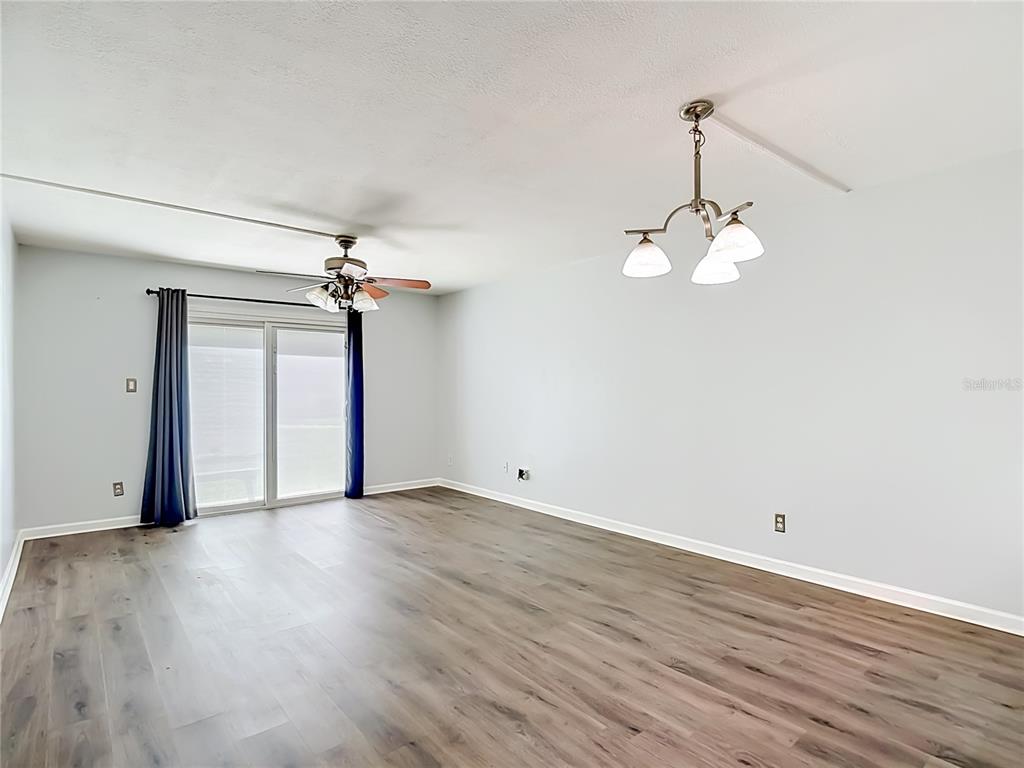 An empty living room features light-colored walls, wood-look flooring, a ceiling fan, and sliding doors — 5820 N CHURCH AVENUE UNIT 164, TAMPA, FL