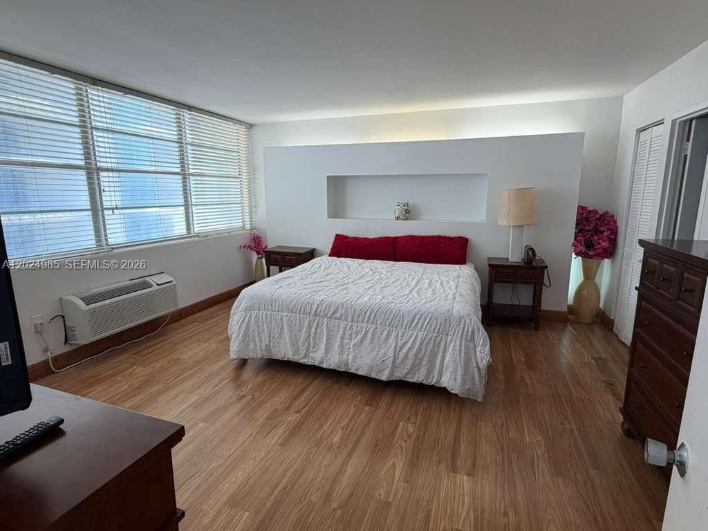 A bedroom features wood-look flooring, a white accent wall with a recessed niche, and blinds — 5313 Collins Ave # 1109, Miami Beach FL 33140, MIAMI BEACH, FL