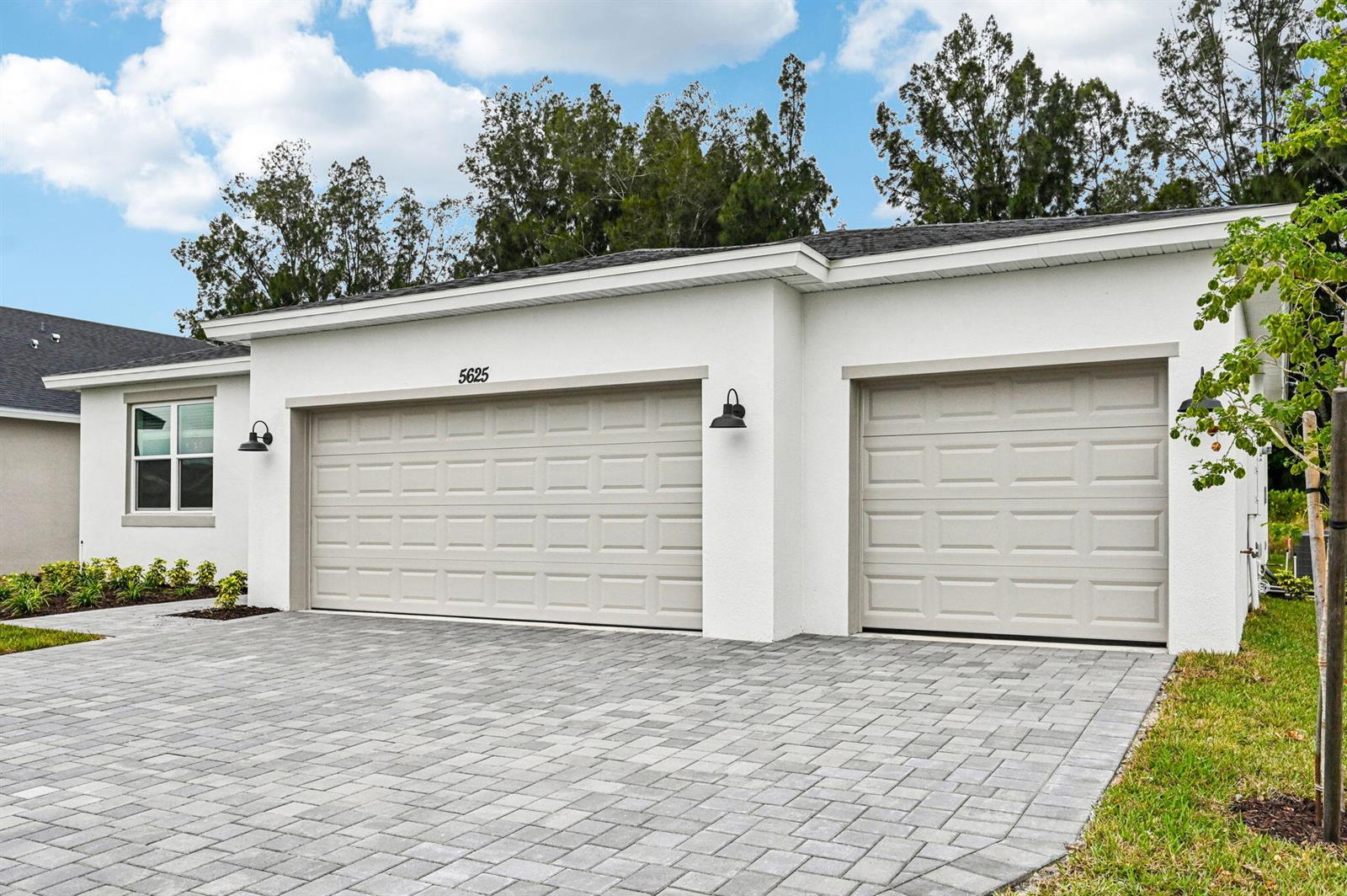 A white house exterior features a three-car garage and a paved driveway — 5625 Hampton Park Circle, Vero Beach FL 32966, VERO BEACH, FL